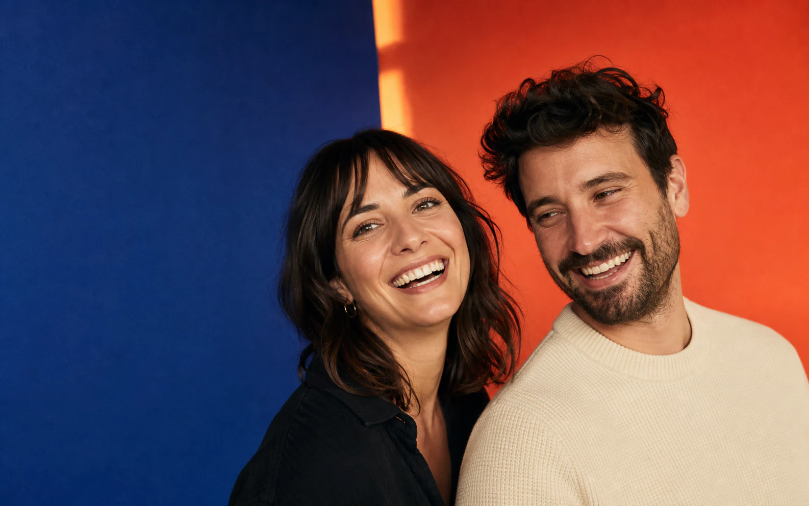 Two friends smiling together against a cobalt and coral background